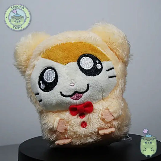 Plush hamster toy with cartoon face in a little bowtie and tiny little hands and feet.