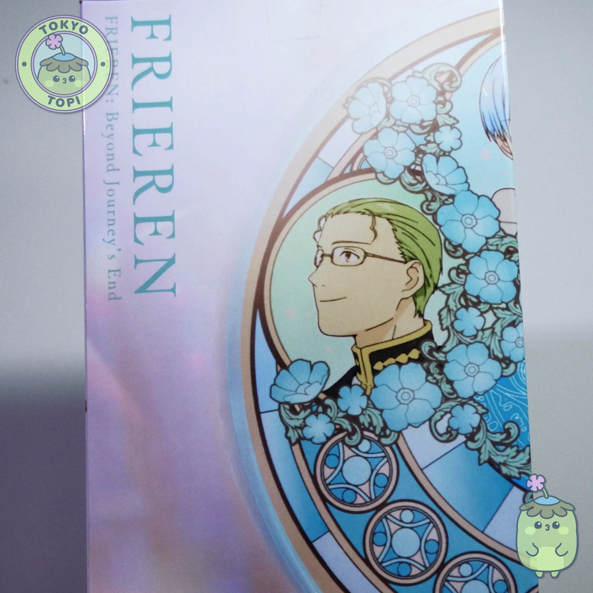 Figure of Frieren from an anime with a stained glass window behind her with other characters from the show including Himmel.