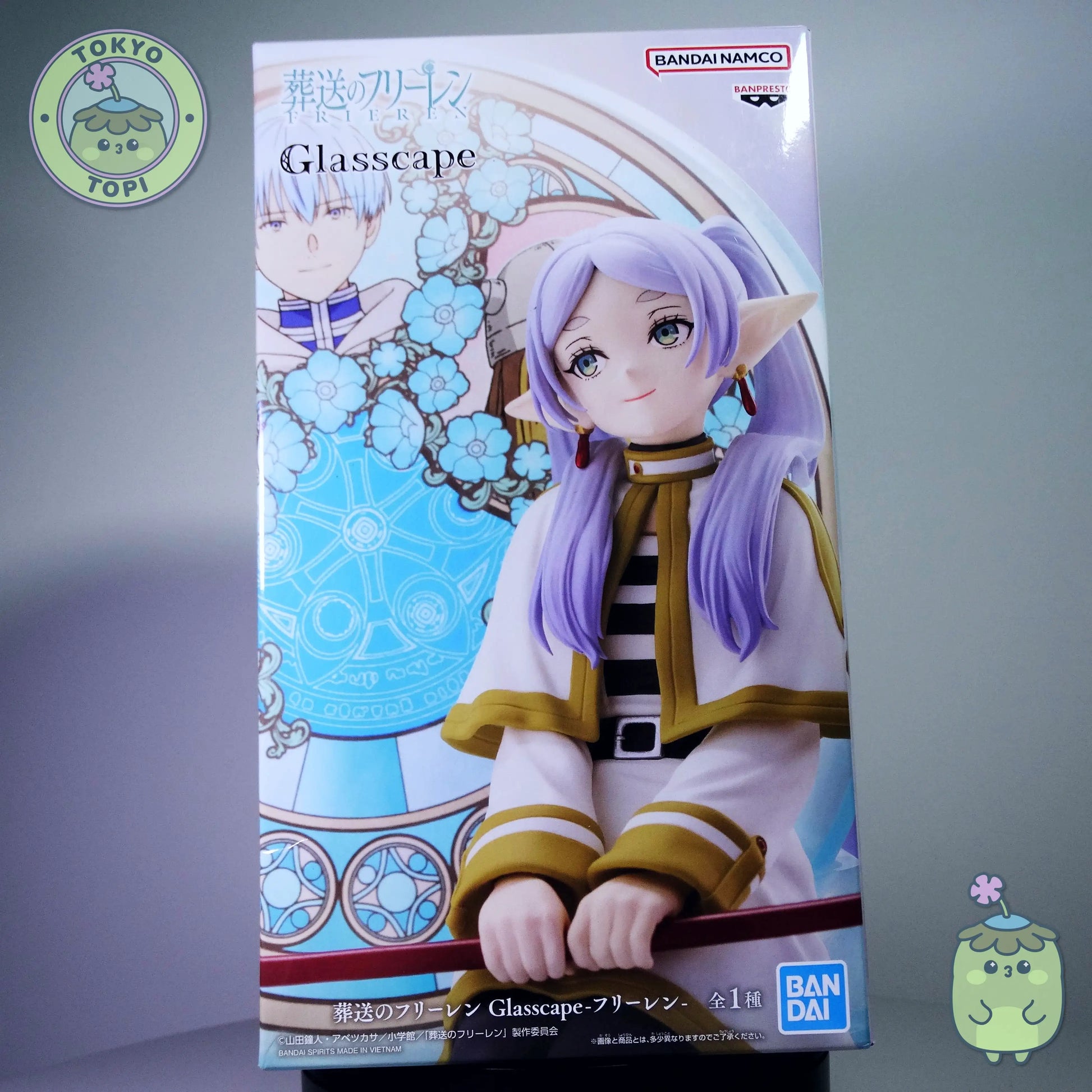 Figure of Frieren from an anime with a stained glass window behind her with other characters from the show including Himmel.