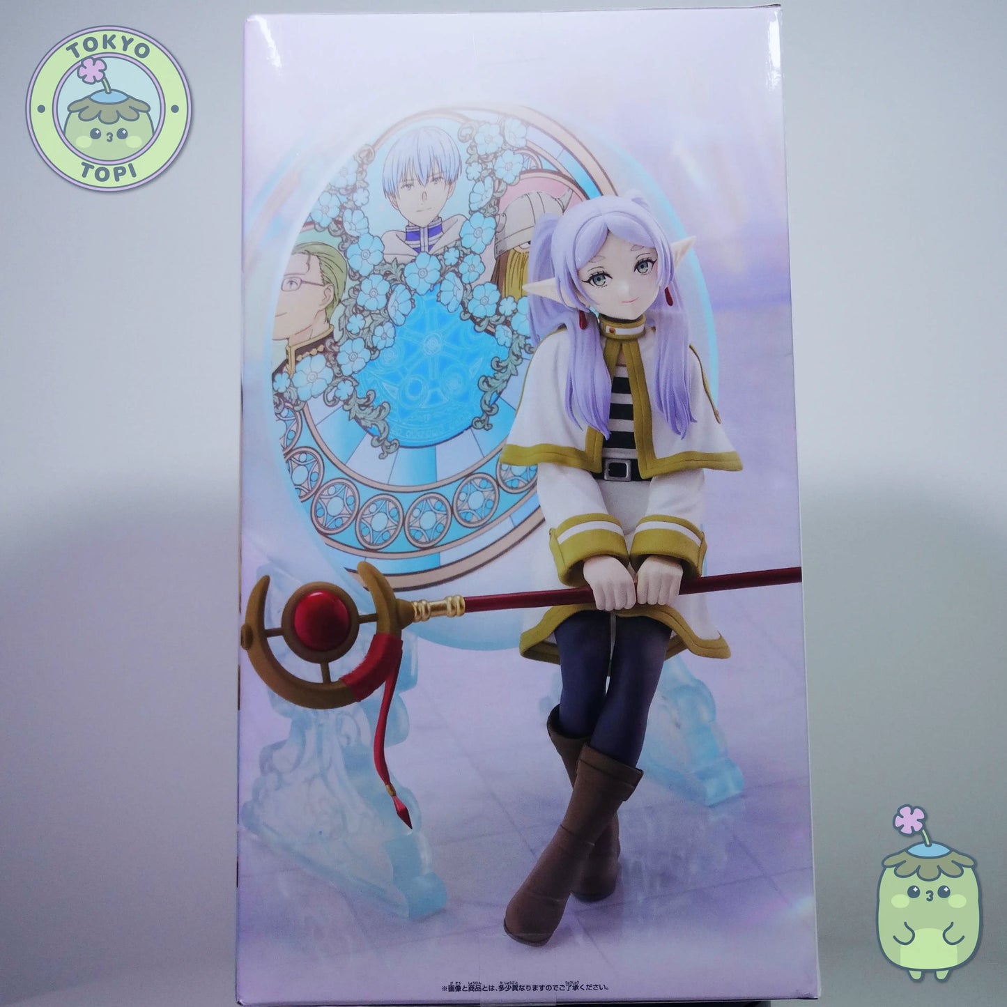 Figure of Frieren from an anime with a stained glass window behind her with other characters from the show including Himmel.